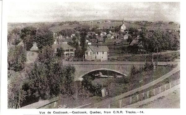 Carte postale illustrant le pont de la rue St-Paul ainsi que la ville de Coaticook. 
Prise de vue de la voie du  chemin de fer C.N.R 